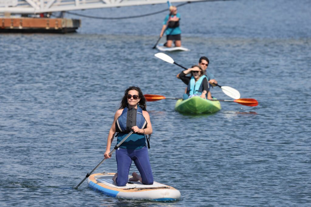 Paddlers on their paddleboards and kayakers paddle through the waters.