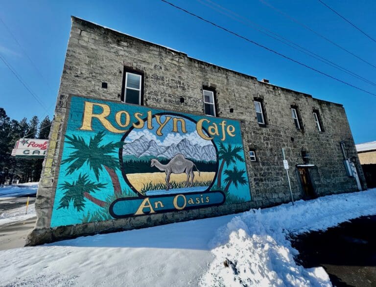 The mural on the side of the Roslyn Cafe is a painting of palm trees, a camel, and a beach.