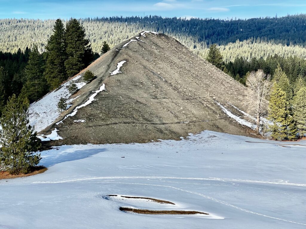 A slag pile from the No. 9 mine sits near the trail surrounded by trees with a few baby trees growing on top of it.