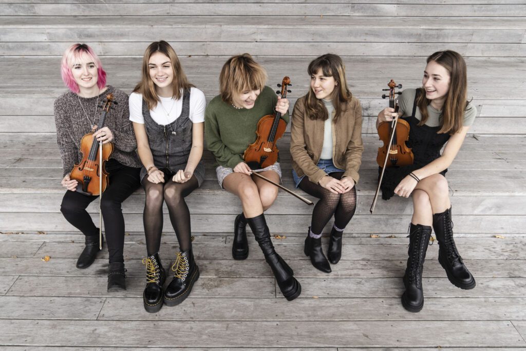 Scottish Fish group laughs and smile as they chat while sitting on the wooden steps with their respective instruments.