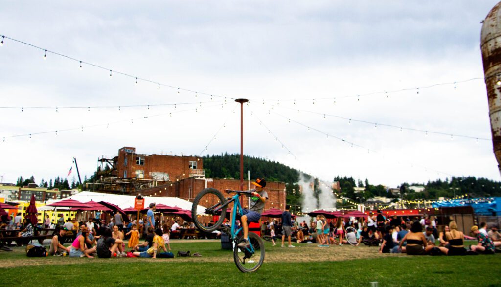 On the lawn of Kulshan Trackside Brewery, young cyclists practice stunts on the grass as many more attendees chat and relax all around him.