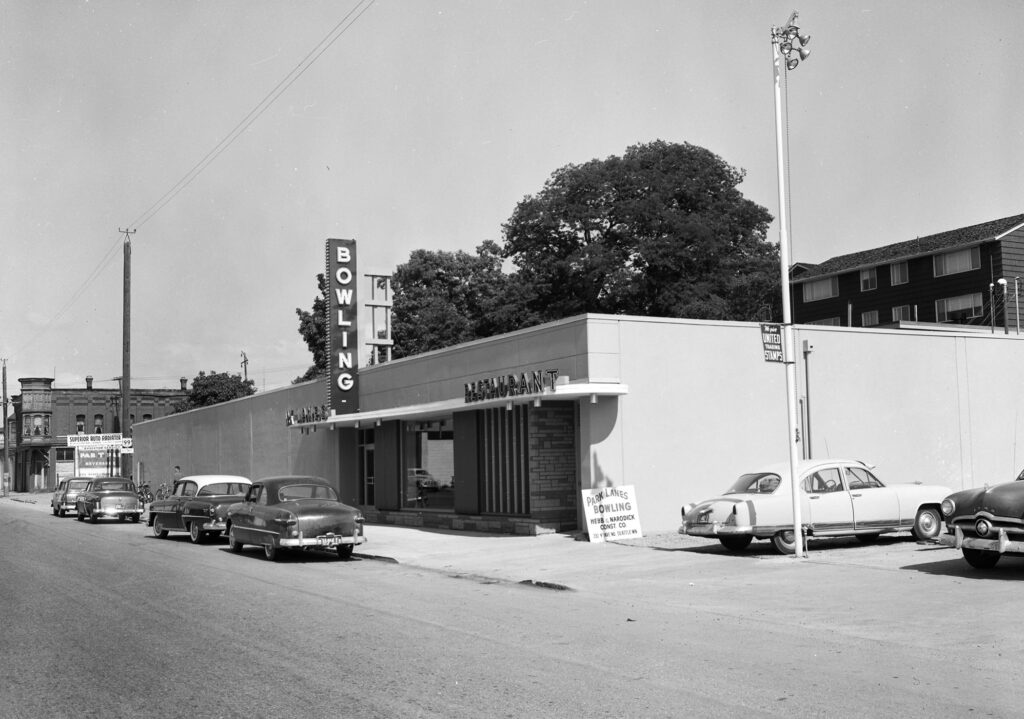 A black and white photograph shows the exterior of an old bowling alley.