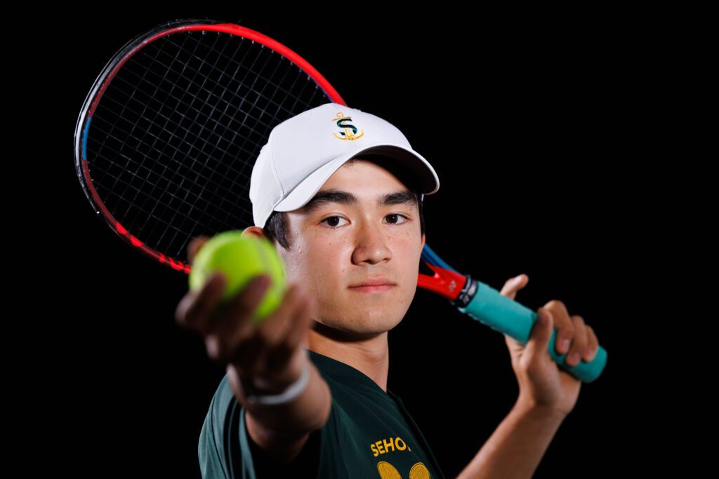 Sehome boys tennis singles player Zach Chai holds out the tennis ball to the camera.