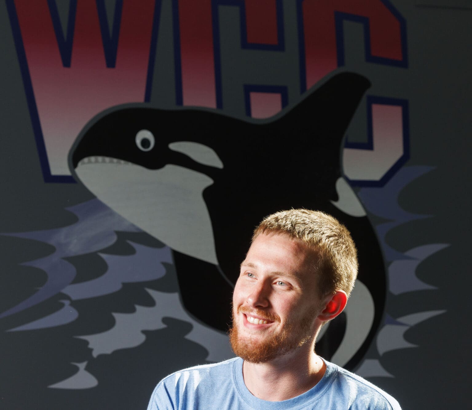 Alex Sommerfield, 25, smiles in front of WCC's orca logo.