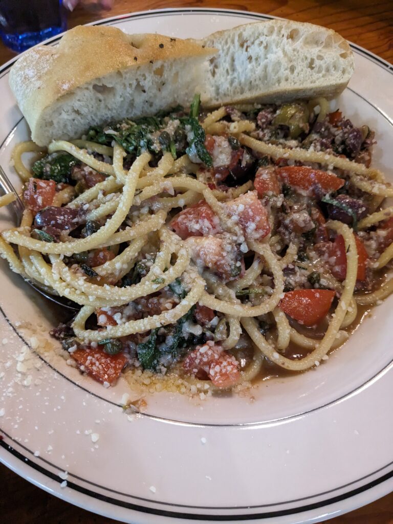 The pasta fresca served with a helping of parmesan cheese and a side of bread on the side of the plate.