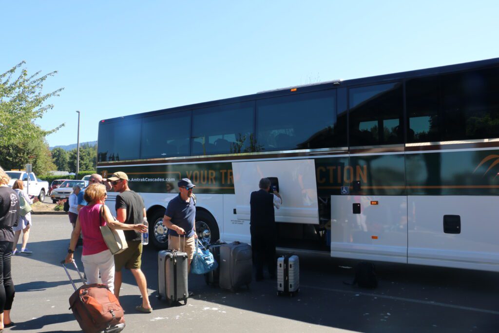 The side of Amtrak’s new electric bus with people idling next to it with their luggages.