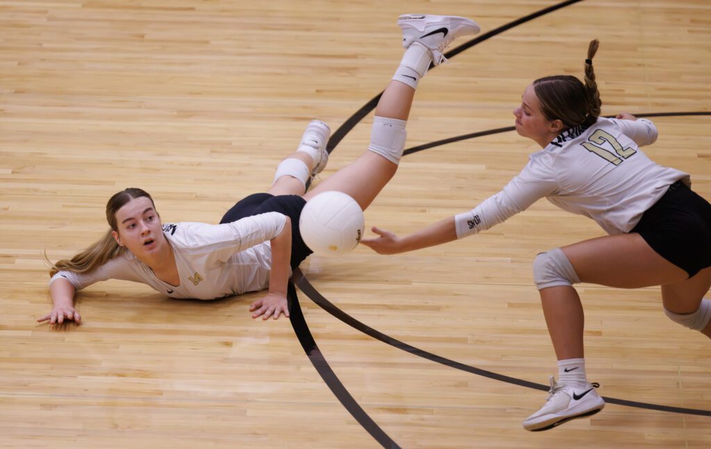 After digging the ball, Meridian's Emry Claeys watches teammate Amelia Koning try to keep the ball in play as she leans forward to reach for the falling ball.