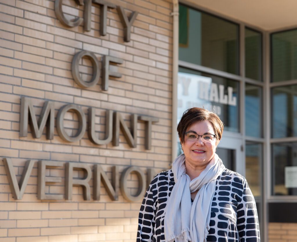 Mount Vernon Mayor Jill Boudreu stands in front of city hall as she smiles for the photo wearing a white scarf.