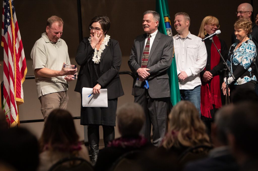 Mount Vernon mayor Jill Boudreau wipes away tears in front of an audience as she receives an award from the police department as others on the stage smile in reaction.