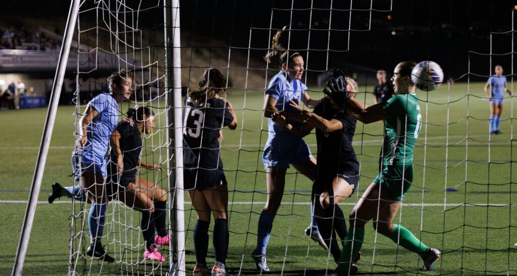 Western's Jayden Nguyen heading the ball in the goal net as other players surround her.