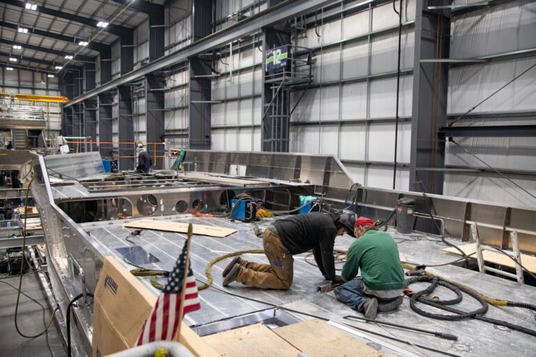 Two men weld the deck of a 52-foot vessel named Gannett surrounded by tools, plank wood and ropes.