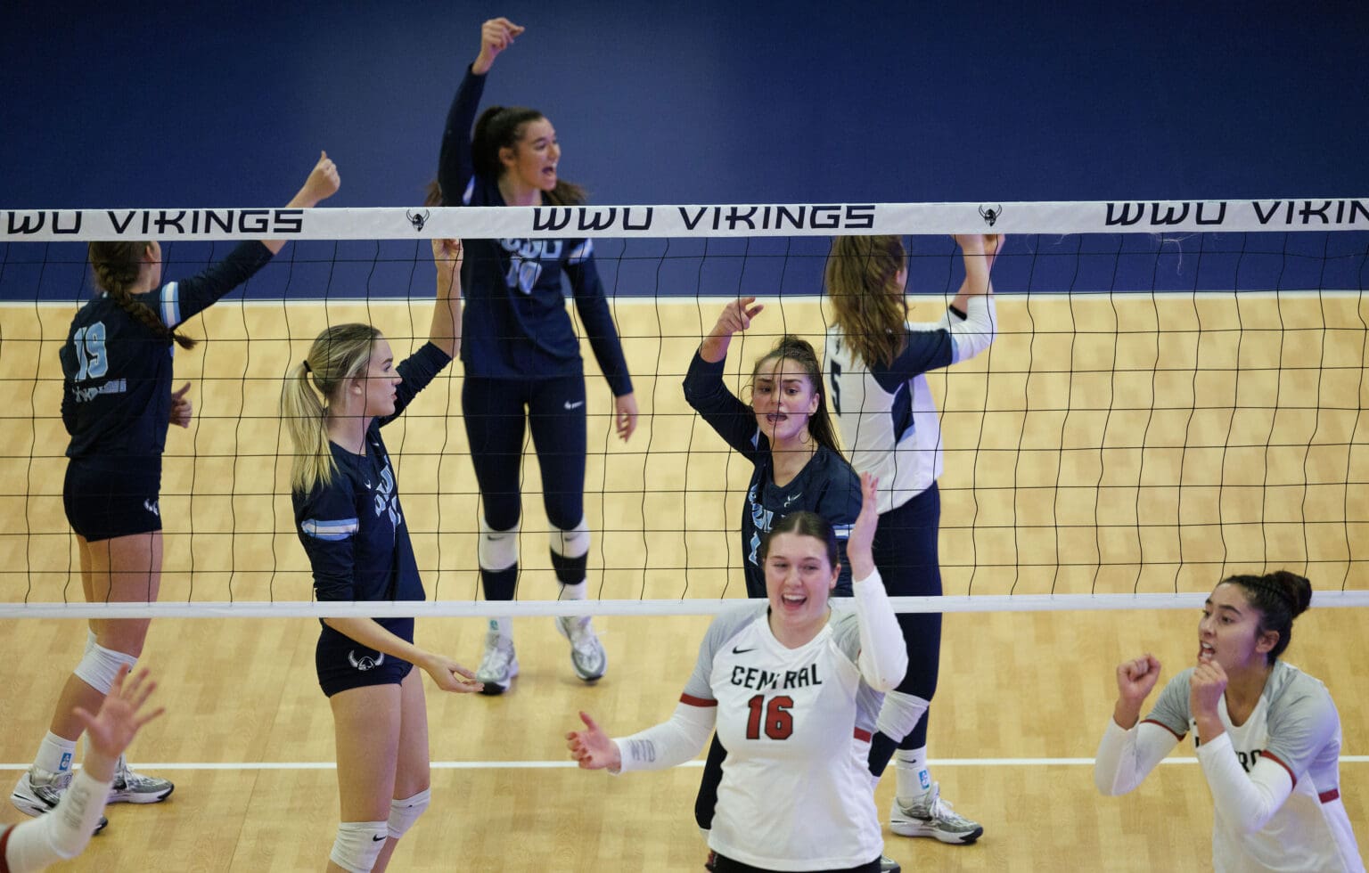 Central Washington University celebrates a point by raising their fits in the air while the Western Washington University players react by arguing the call.