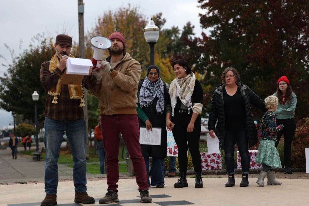 Erum Mohiuddin and Asch Qattawi hold hands in support as speaker Yoav Litvin talks through the megaphone as he addresses the crowd present.