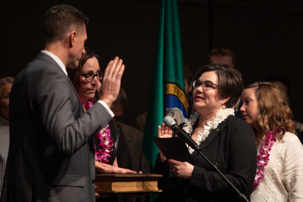 Jill Boudreau swears in Peter Donovan, left, as the next mayor of Mount Vernon surrounded by her peers on the stage, next to the state washington flag.