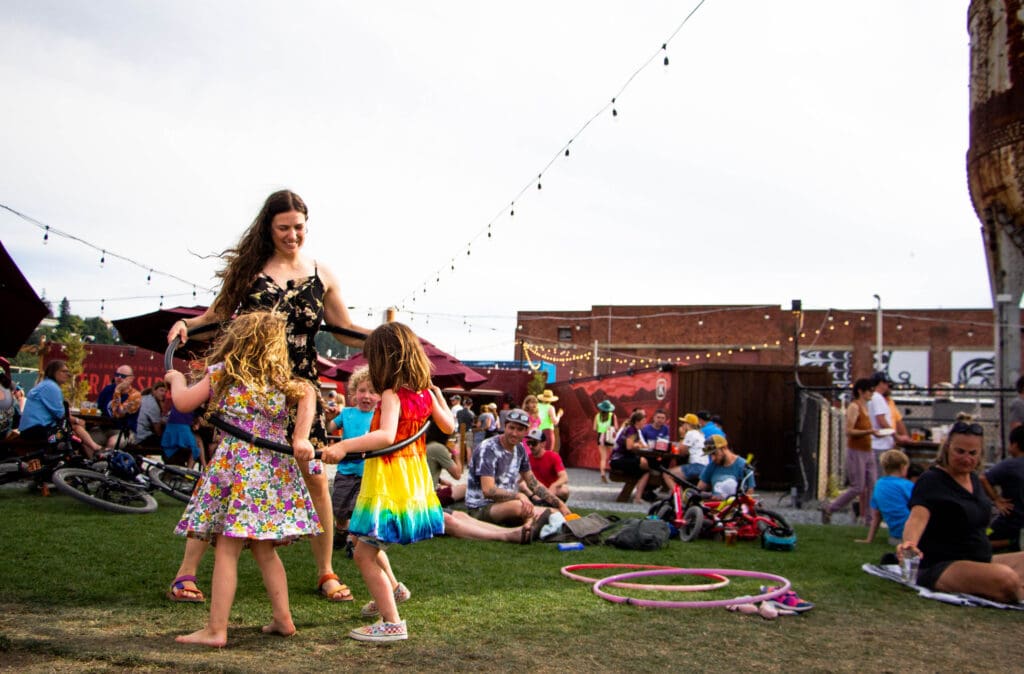 Stephanie Short teaches Emmeline and Sonny how to hula-hoop at Trackside Beer Garden as a crowd sits nearby chatting.