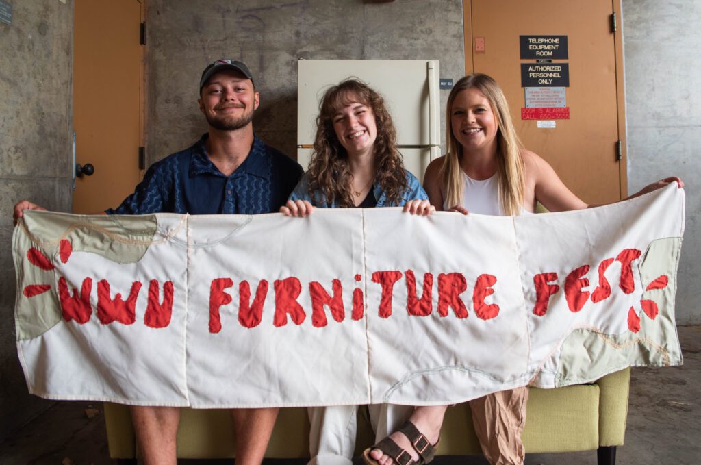 From left, Thane Davis, Nikita Presler and Amber Olsen hold a Furniture Fest banner made from recycled fabrics from Western Washington University's Commissary building where all the furniture is stored.