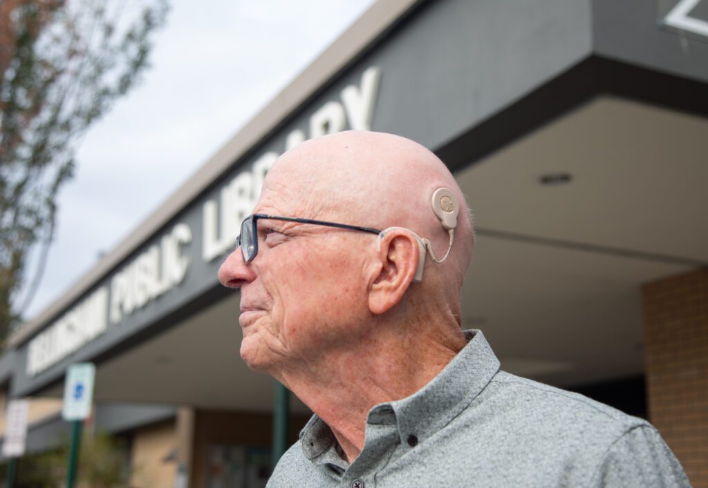 Larry Wonnacott shows his cochlear implant that sticks to the side of his and loops to the back of his ear.