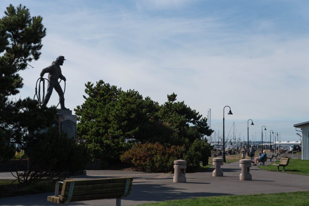 The Fisherman's Memorial, left, stands at Zuanich Point Park as many visitors walk along the path with some sitting on benches to admire the view.