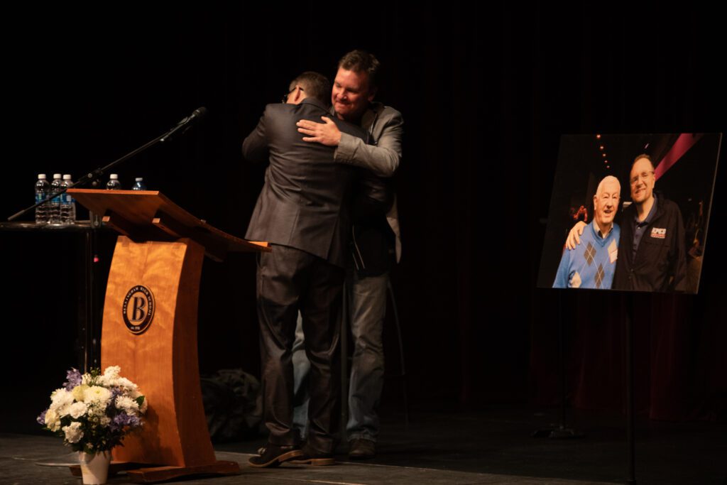 KPUG sportscaster Rick Todd, left, hugs Michael Scholten, Mark's brother, on stage during the celebration of life.