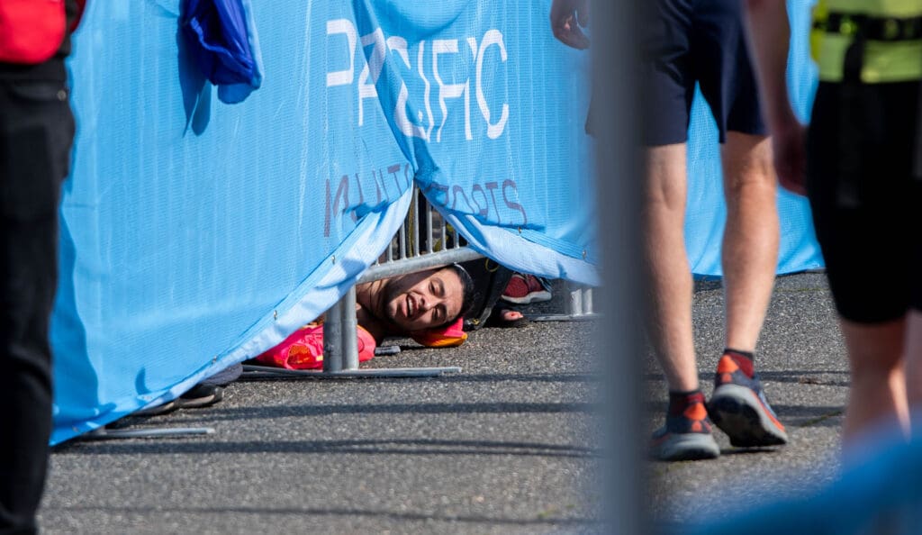 Ian Cervantes cheers on runners from under the barricade and the blue banner at the finish line.