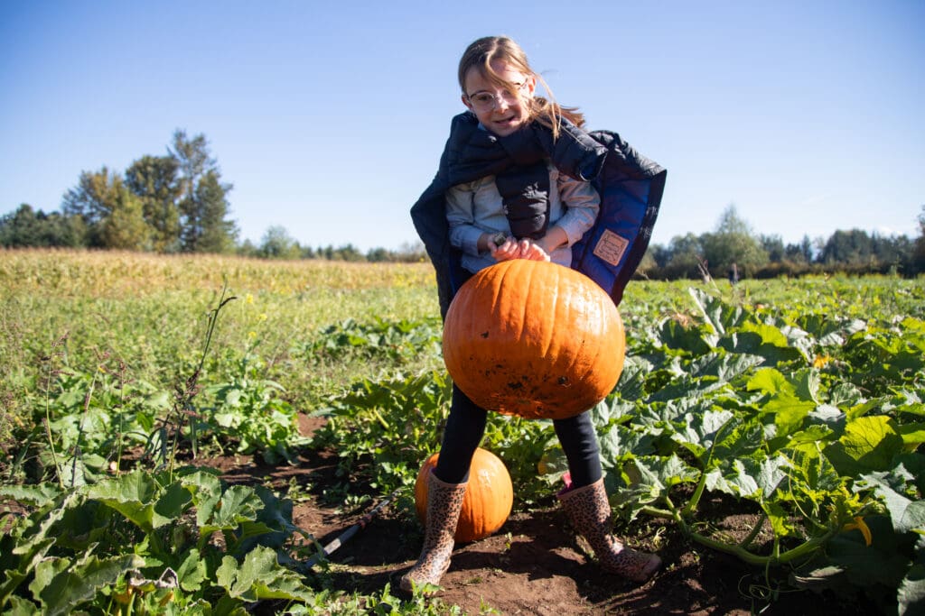 Stella Sullivan holding up a pumpkin in the middle of the pumpkin patch.