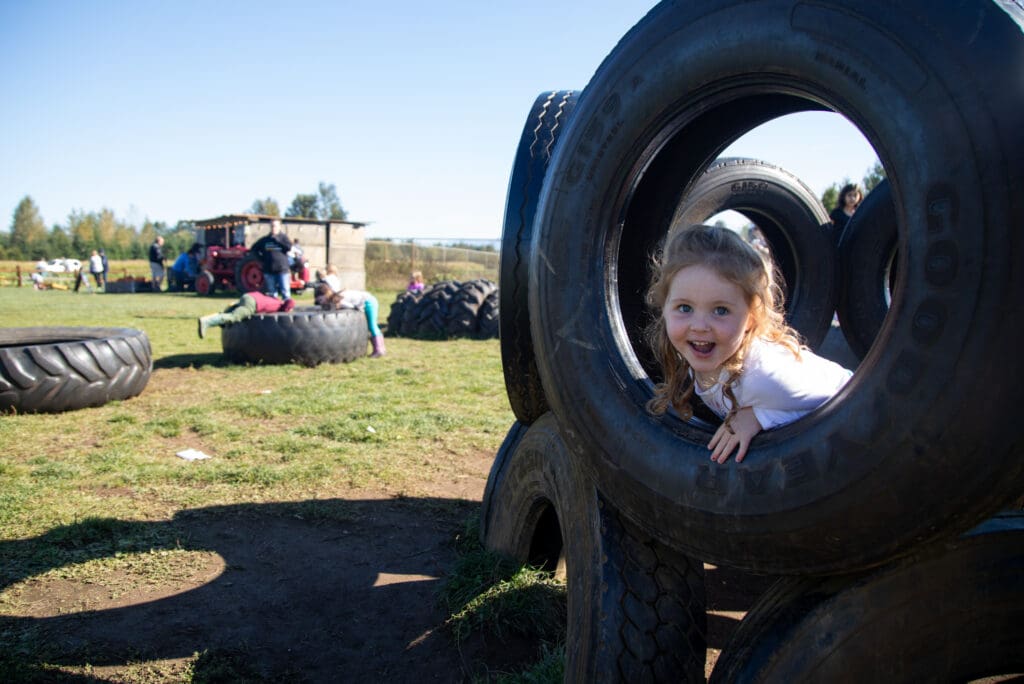 Claire Fennell climbs through the tire playground with a smile as other children play with large tractor tires in the background.