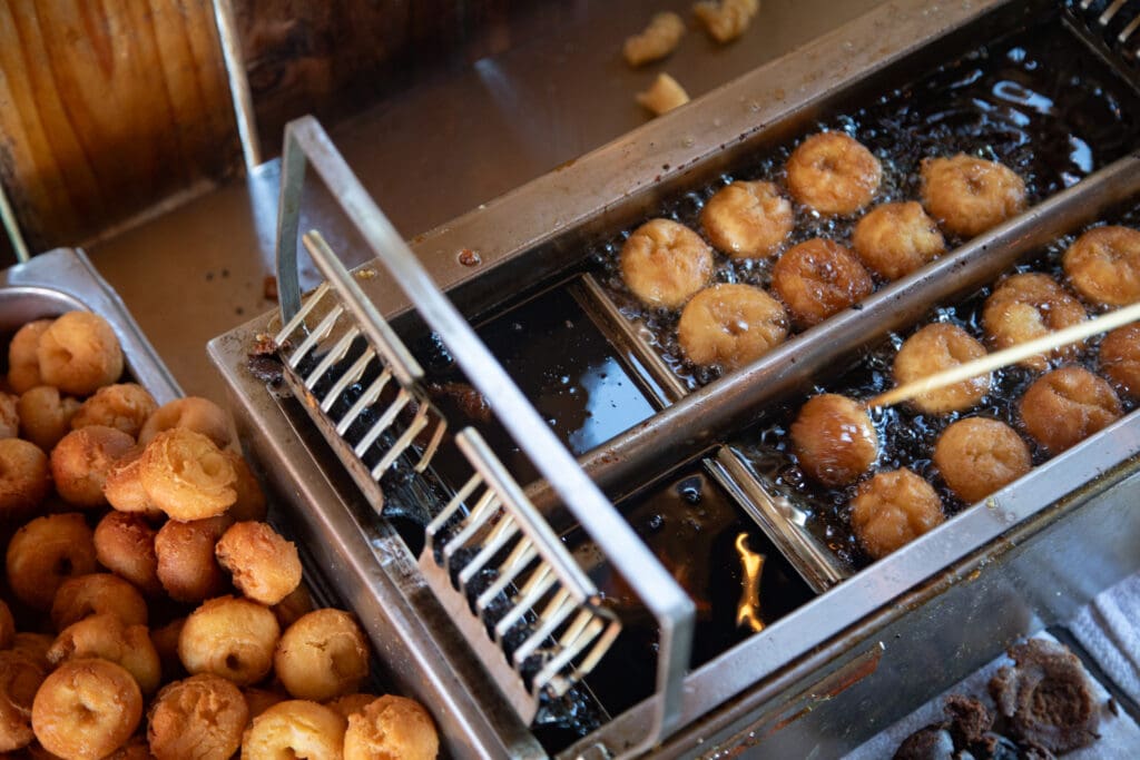 Tami Jefferson flips apple cider doughnuts as they fry as a batch of golden-brown sits idling next to the fryer.