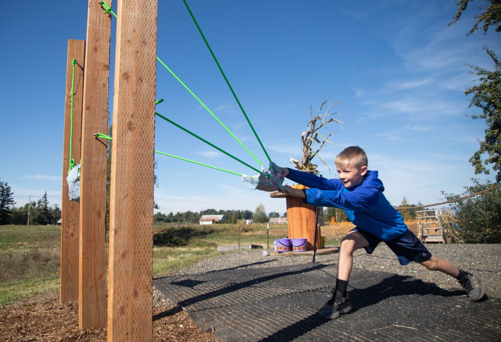 Louise DeVries' grandson Kellen, 8, pulls back a green slingshot to launch a mini pumpkin.