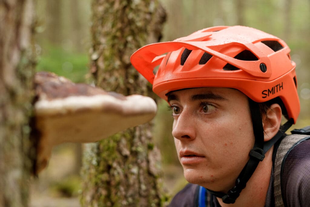 Talus Lantz examining a shelf fungi sprouting from the tree while wearing an orange cycling helmet.