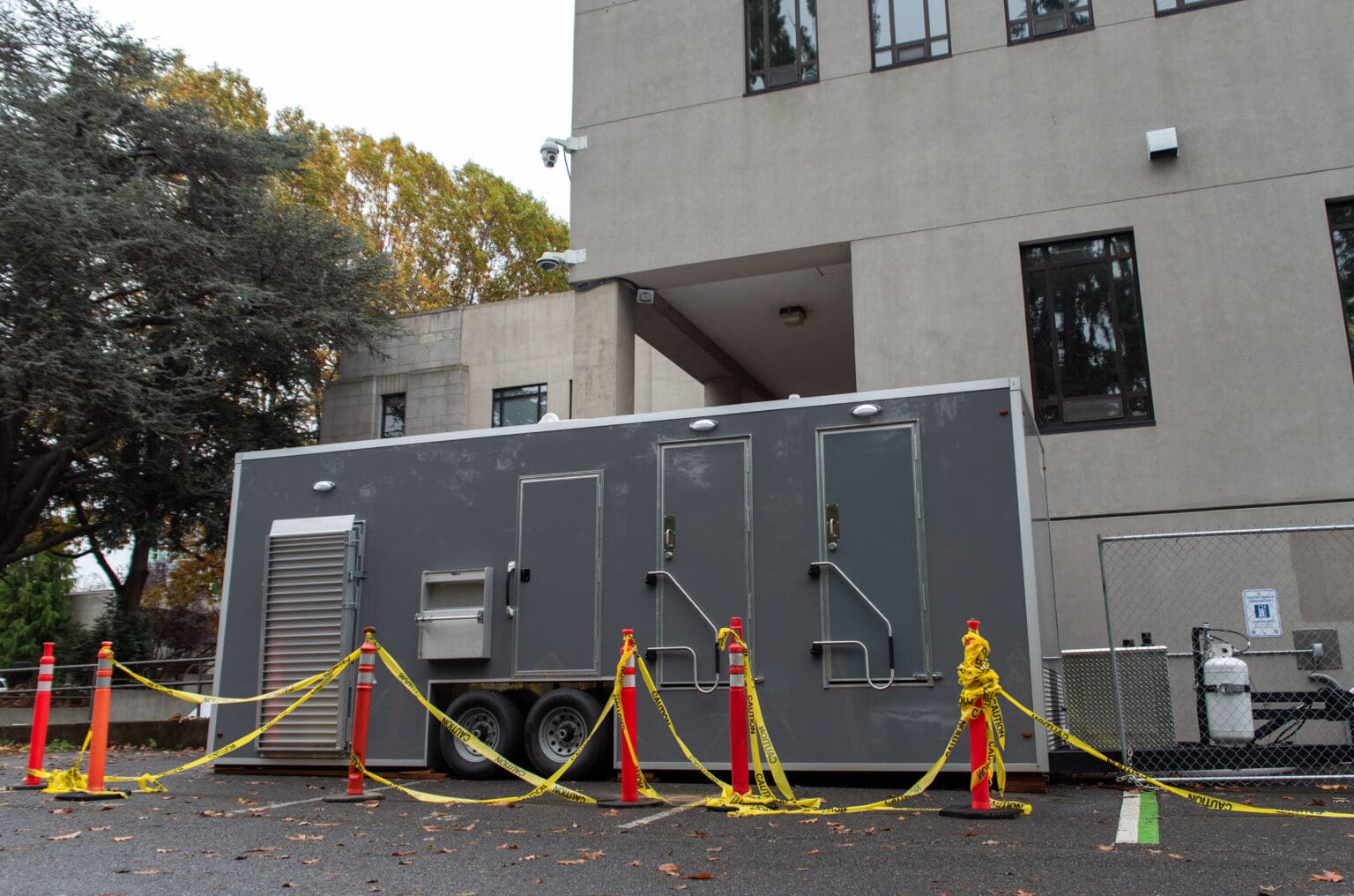 A mobile shower trailer parked next to a white building is taped off from public access.