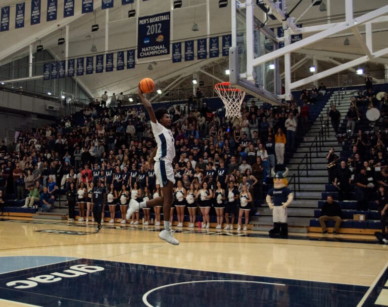 Western men's basketball senior Darius Gary takes off from the ground to dunk the basket as spectators watch from the sidelines.