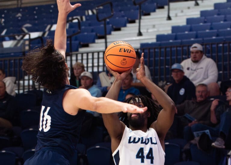 Junior guard Will Wilson leaping to take a shot as another player tries to block.