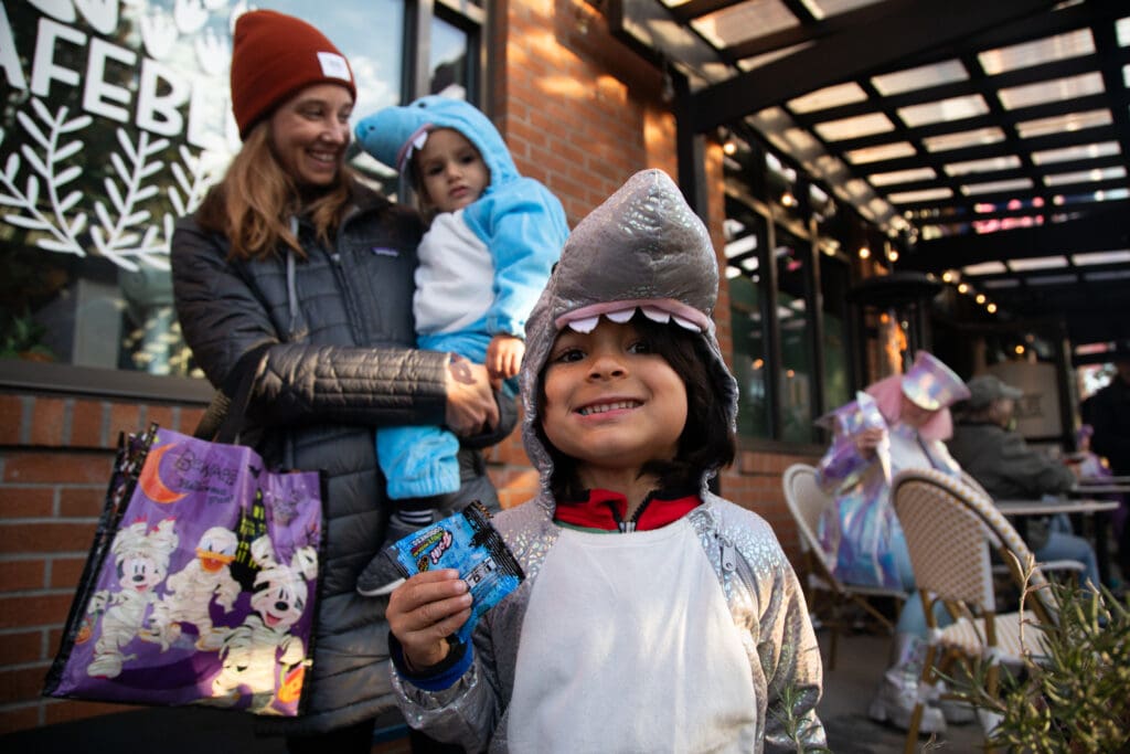 Ryden Fernandez shows off a pack of gummies as he's dressed in a shark onesie while his mom and sister are behind him.