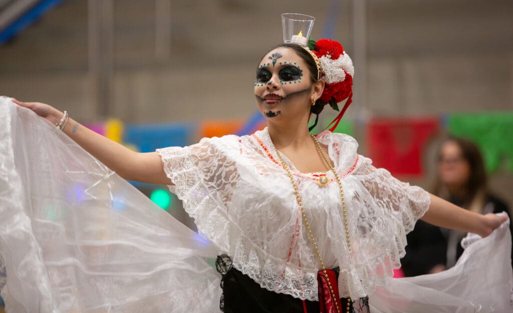 Carla Hernandez performs with a glass containing a lit candle as she holds onto the sides of her white dress in the air.