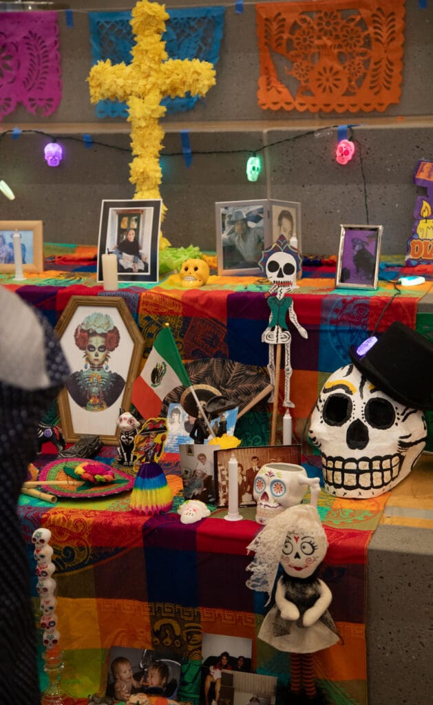 The altar for el Día de los Muertos features photos and notes honoring loved ones who've passed on decorated with multicolored designs and cloth.