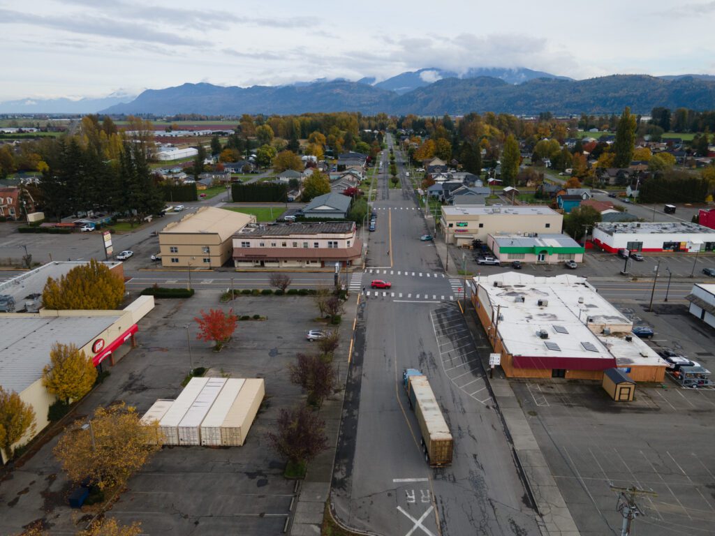 A truck and car drive through Garfield street surrounded by businesses and other parked cars.