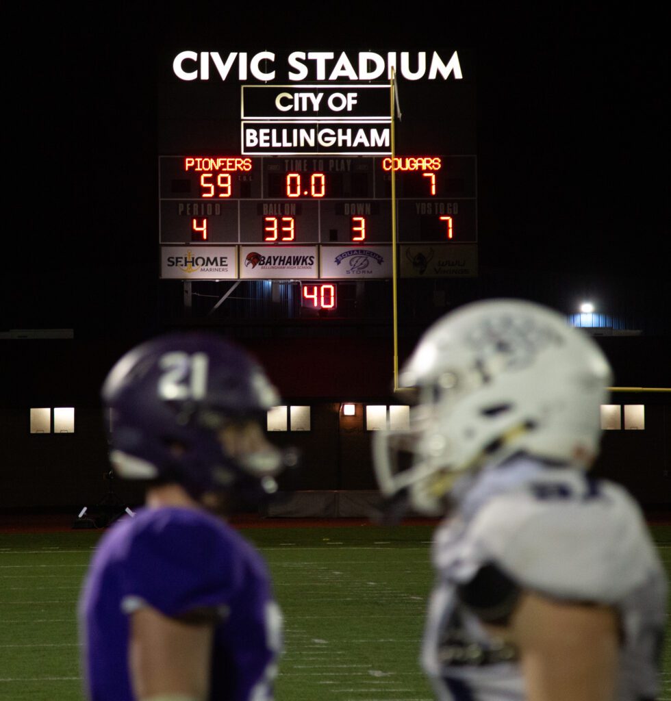 Players shake hands as a bright signboard looms over the field.