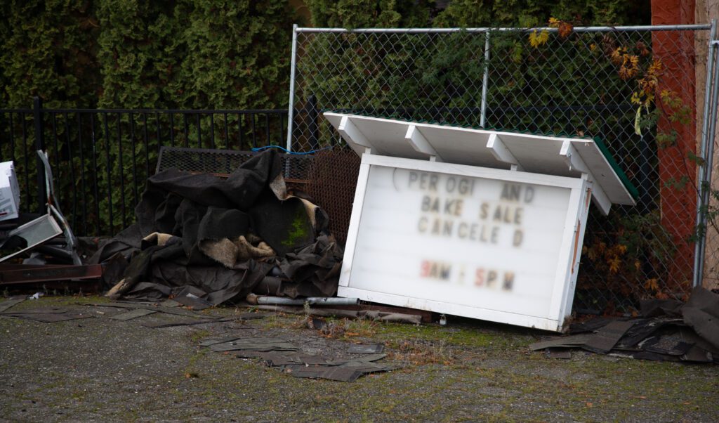 A message board sits leaning against the fence on the church's grounds and advertises the canceled pierogi and bake sale lies next to other debris and garbage.