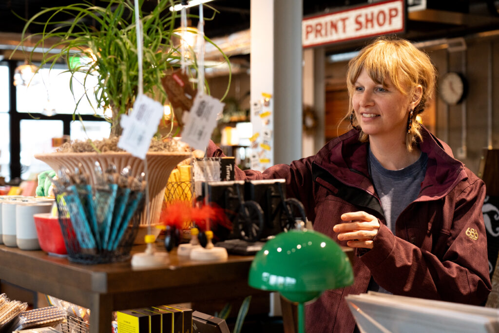 Angela Cook reaches for an item on the wooden shelf showcasing the product at the Bison Bookbinding & Letterpress inside the Granary Building