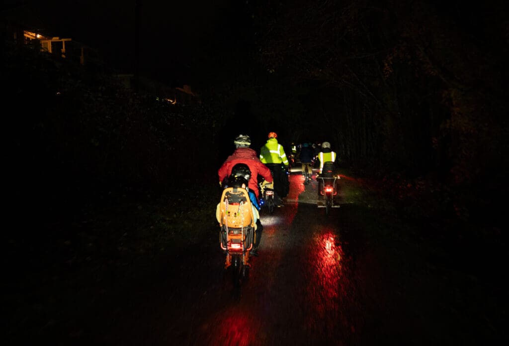 Cyclists on cargo e-bikes bike along the interurban path. Cyclists were dressed in rain and safety gear to attempt to stay dry on the wet night.