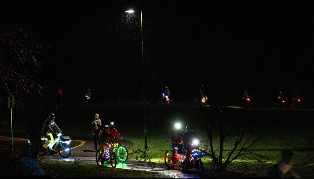 Cyclists riding their brightly lit bicycles circle the asphalt path that circumnavigates Boulevard Park in Fairhaven.