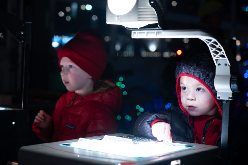 Children create different patterns on an old projector. A bright light shines down on a panel meant to showcase the pictures.