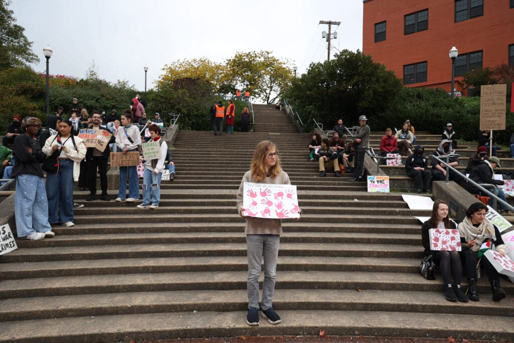 Nathan Farnorth holds a sign reading 'they are all our children' with red children hand marks.