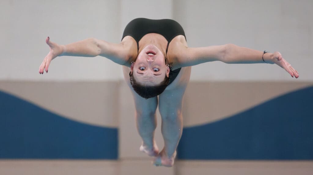 Sehome’s Samantha Toepper upside down as she performs a backwards dive with her arms stretched outwards.