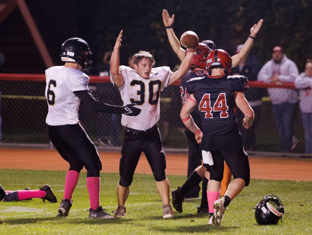 Meridian's Josh Elmer signals a touchdown after having his helmet pulled off by another player as others also signal the same way with their hands up in the air.