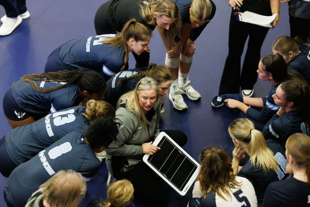 Western head coach Diane Flick-Williams talks with her team during a timeout pointing to a clipboard in her hand.