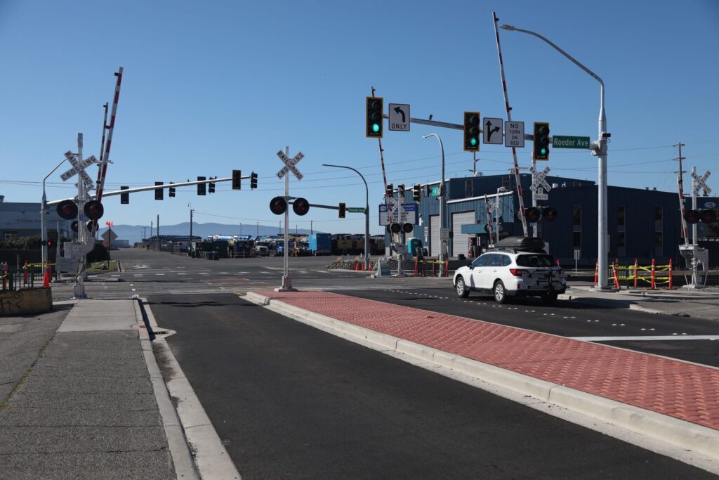 The railroad crossing at F Street where a car is about to leave as the traffic lights turn green.