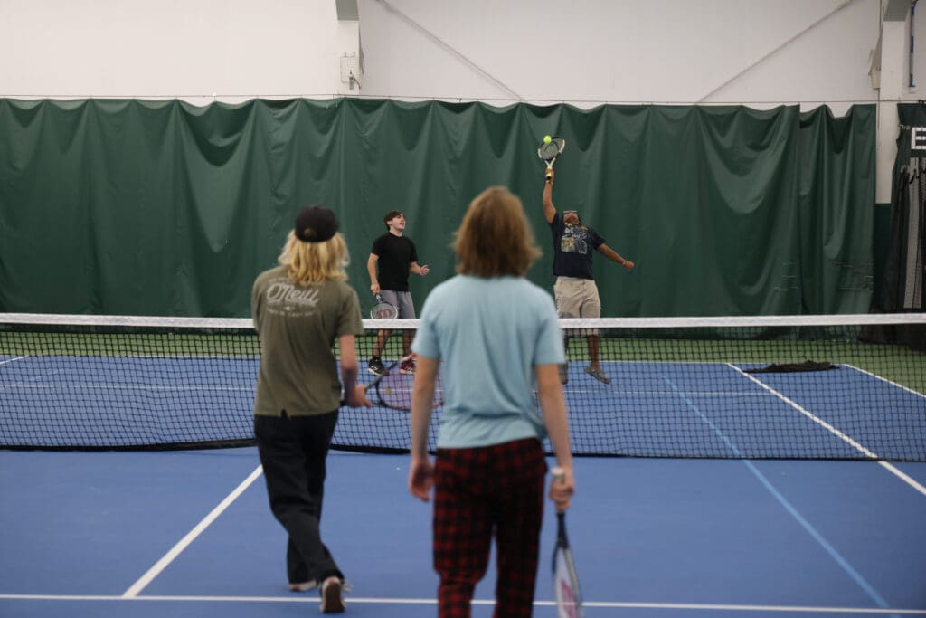 Friends of Lucy Guerra play doubles tennis as one of them prepare to serve.