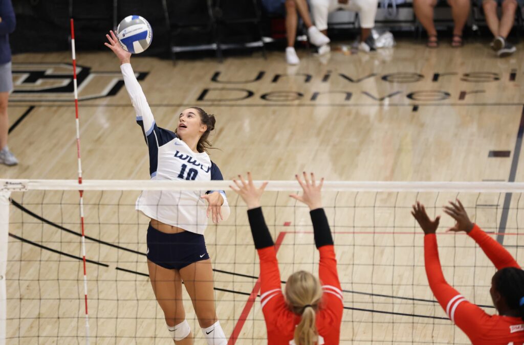 Western Washington University's Devyn Oestreich reaches out to the ball to spike it over the net as two defenders leap to block the shot.