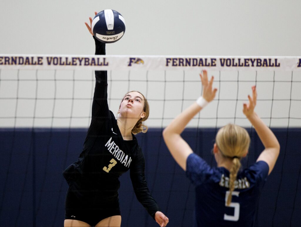 Meridian's Emry Claeys spikes the ball over the net as a defender gets ready to block the shot.